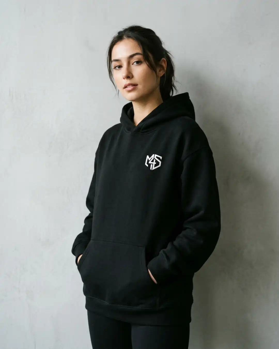 Off Autopilot Hoodie – Wear – Female Female model wearing the black Off Autopilot Hoodie in a minimalist concrete setting