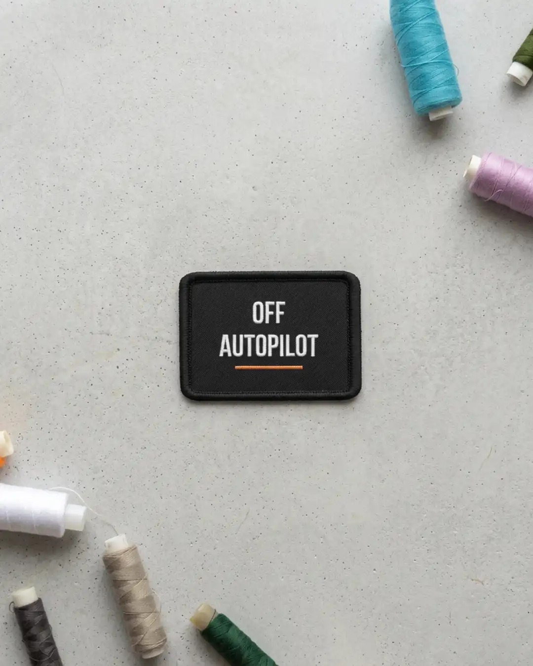 Off Autopilot Patch – Product Detail Off Autopilot embroidered patch shown against a concrete surface with sewing threads around it